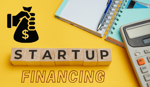 Startup Financing concept with blocks spelling 'STARTUP,' a calculator, notebook, and a hand holding a bag of money.