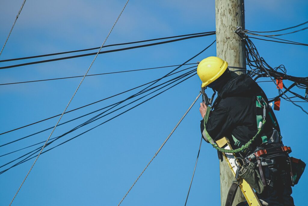 Electrician with a yellow hard hat working on power lines, demonstrating the hands-on work of electrical contractors